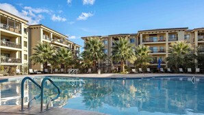 Une piscine entourée de bâtiments à plusieurs étages dotés de balcons, avec des chaises longues et des palmiers.