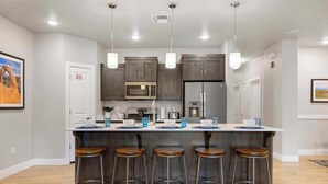 Une cuisine moderne dotée d’un îlot central, de tabourets de bar et de luminaires suspendus.