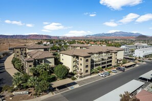 A multi-story hotel with a parking lot, surrounded by mountains and a clear sky.
