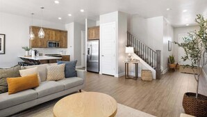A modern living room with a sofa, a round coffee table, and a kitchen area with wooden cabinets and stainless steel appliances.