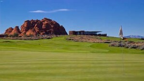 A golf course with a flagstick, a building, and a large rock formation in the background. - Sweet Retreat | Rest & Relax Near National Parks (Hurricane)