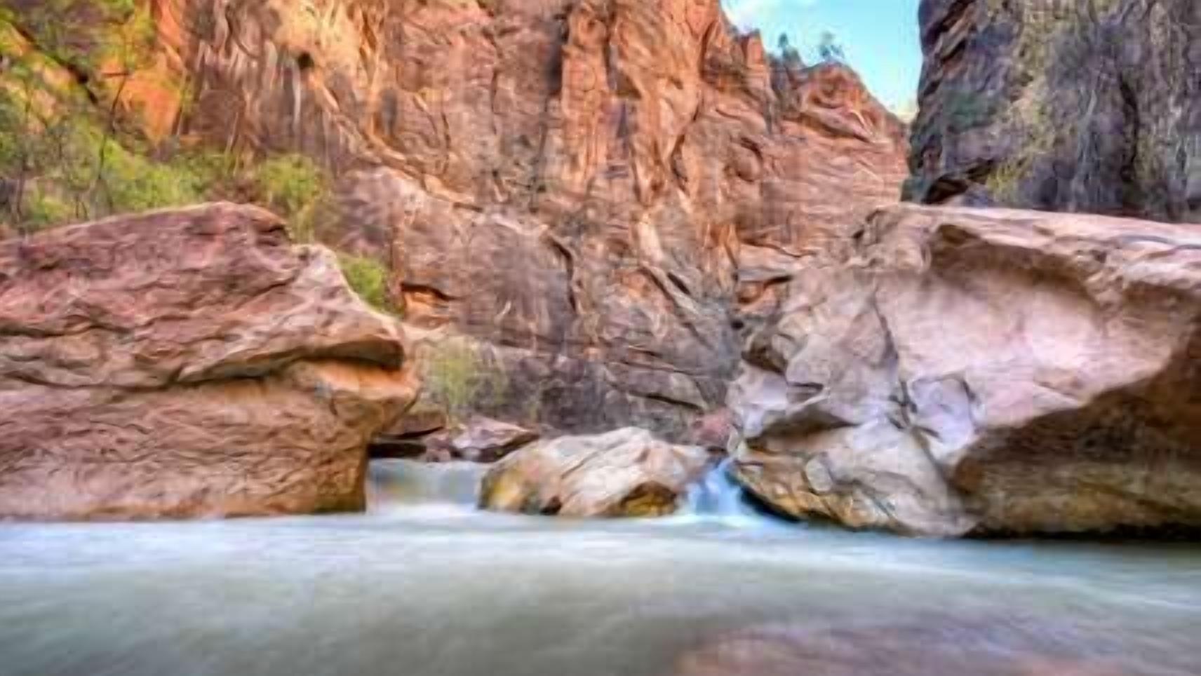 A river flowing through a rocky canyon with large boulders and a clear sky.