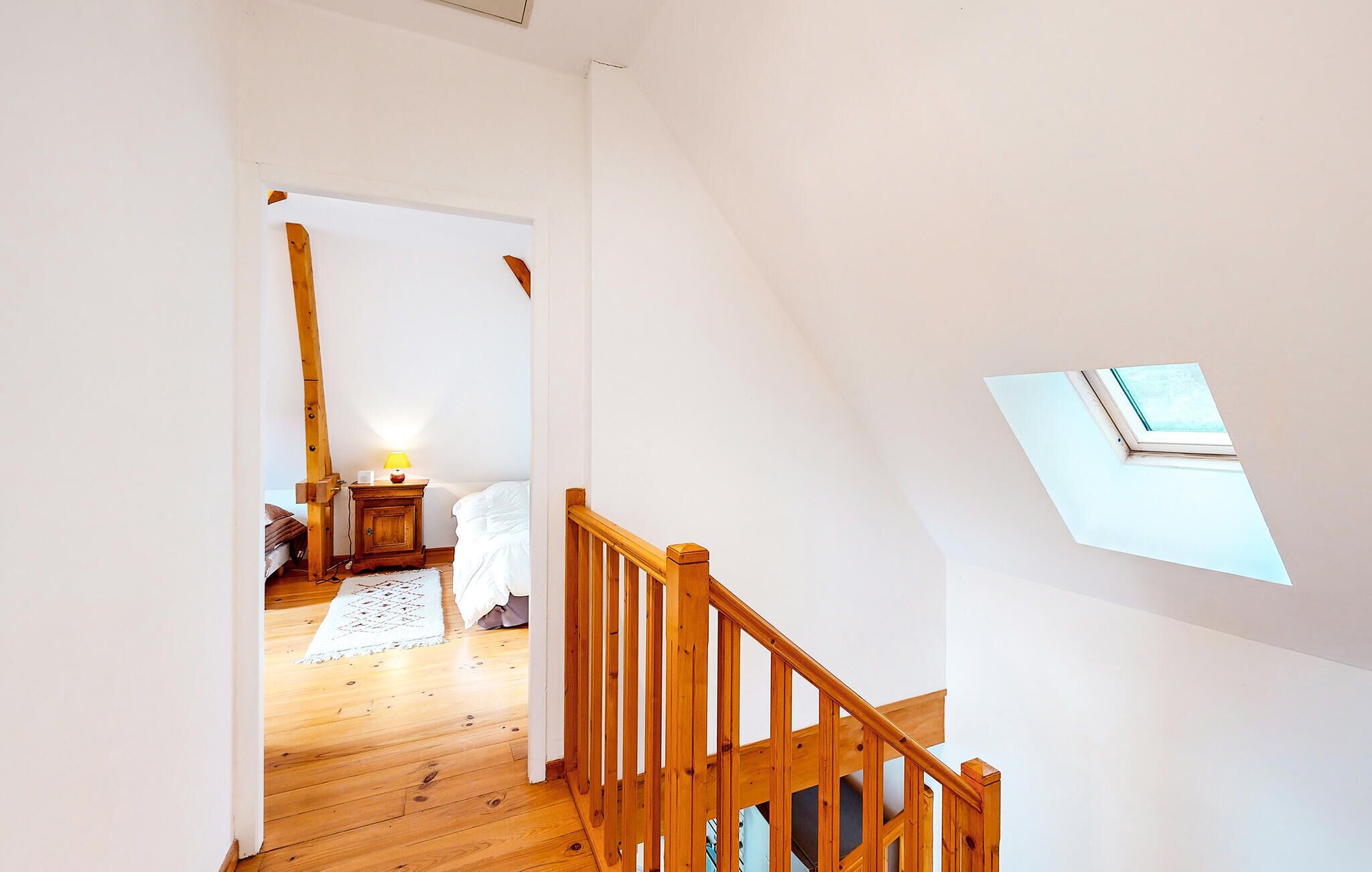 Eine Holztreppe mit Geländern führt zu einem Schlafzimmer im Zwischengeschoss mit Dachfenster.