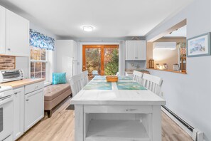 A modern kitchen with white cabinetry, a wooden countertop, and a dining area with a white table and chairs.