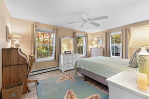 A bedroom with a bed, dresser, vanity, and a ceiling fan.