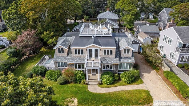 Une grande maison à plusieurs étages, dotée d’un balcon imposant, entourée d’une végétation luxuriante et d’autres immeubles résidentiels.