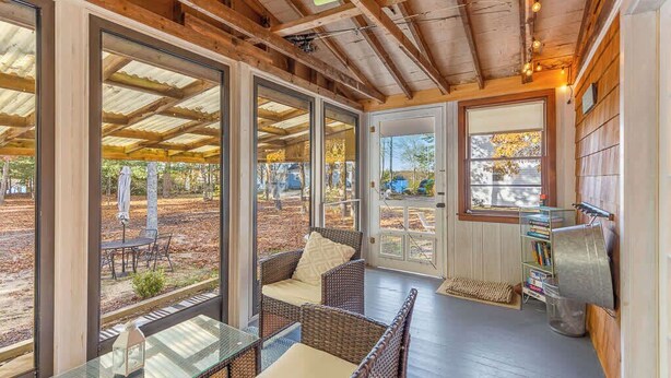 A covered porch with wicker furniture, a glass table, and a bookshelf. - Cappawack Cottage | Firepit & Private Beach Nearby (Mashpee)