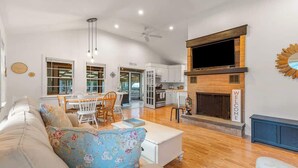 A modern living room with a sofa, a dining area, and a kitchen. - Cappawack Cottage | Firepit & Private Beach Nearby (Mashpee)