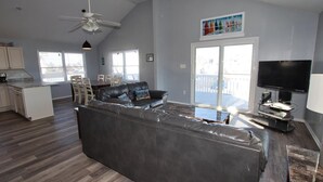 A spacious living room with a large L-shaped sectional sofa, a flat-screen TV, and a dining area with wooden chairs.
