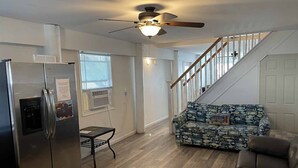 A spacious living area with a modern kitchen, a patterned sofa, a leather couch, and a staircase leading to an upper level.