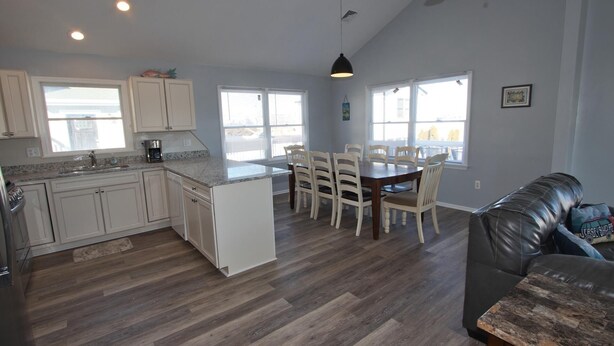 A spacious kitchen with white cabinets, a dining area with a wooden table and chairs, and a leather couch in a modern living room.