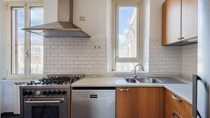 A kitchen with a gas stove, oven, dishwasher, wooden cabinets, and a window. - Vittorio Panoramic Apartment (Roma)