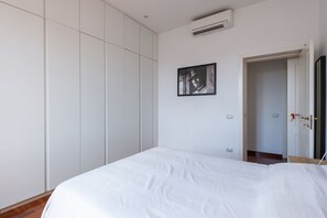 Une chambre à coucher comprenant un lit, une armoire, un appareil de climatisation et une porte donnant sur une autre pièce.