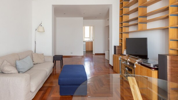 A modern living room with a sofa, ottoman, TV, and wooden shelving unit. - Vittorio Panoramic Apartment (Roma)