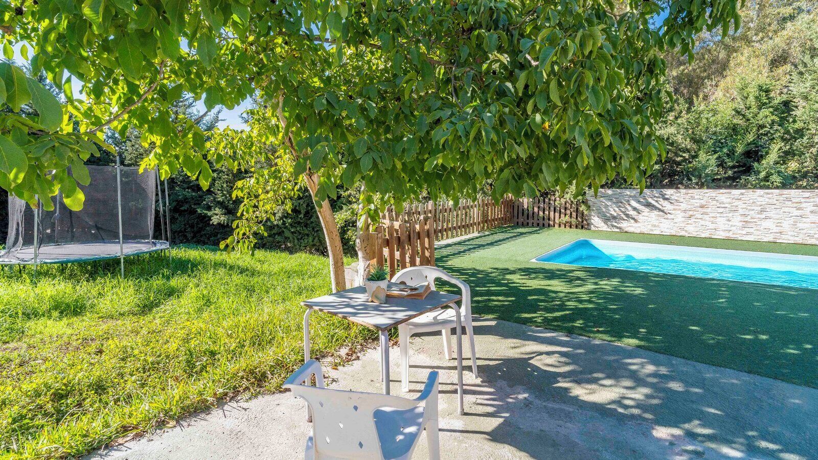 Un jardin avec un trampoline, une petite table et des chaises, et une piscine.