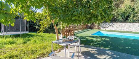 Un jardin avec un trampoline, une petite table et des chaises, et une piscine.