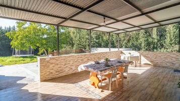 Un área de comedor al aire libre cubierta con una mesa dispuesta para dos personas, rodeada de muros de madera y vistas a un bosque.