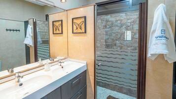 Un baño moderno con lavamanos doble, cabina de ducha de vidrio y cuadros con mariposas en la pared.