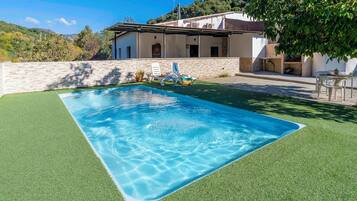 Una piscina rectangular con agua azul cristalina, rodeada de césped artificial verde.