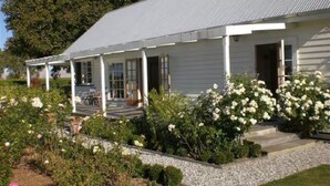 Un bâtiment blanc doté d’un porche, entouré d’un jardin où poussent des fleurs et des arbustes blancs.