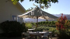 Une terrasse avec une table et des chaises, protégée par un grand parasol, entourée de verdure et offrant une vue sur la montagne.