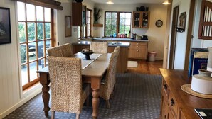 Une cuisine chaleureuse avec une table à manger en bois, des chaises en osier et une fenêtre donnant sur un espace verdoyant.