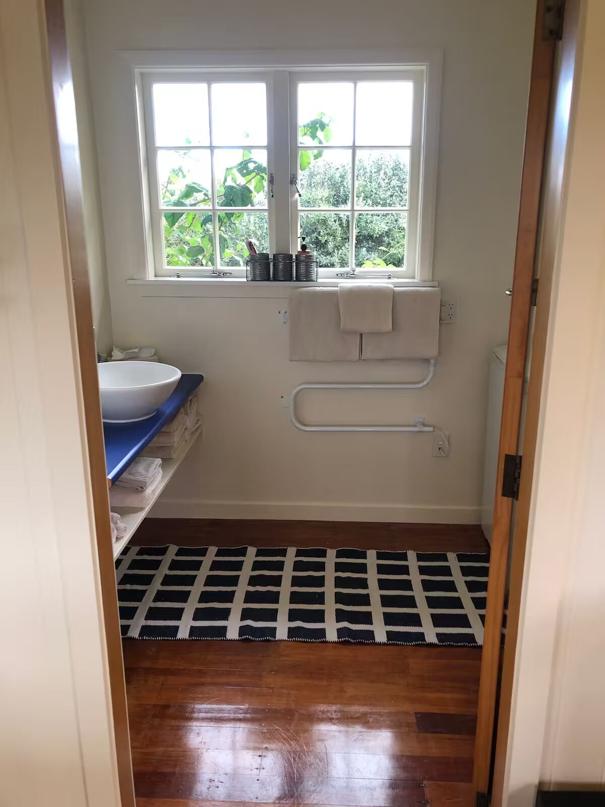 A small bathroom with a window, a white sink, a towel rack, and a patterned rug on the floor.