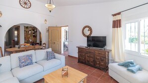 En stue med en sofa, et sofabord, et fjernsyn på et træskab, samt et spiseområde med et bord og stole.