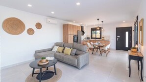 Een moderne woonkamer met een grijze bank, een ronde salontafel en een eethoek met een zwarte deur.