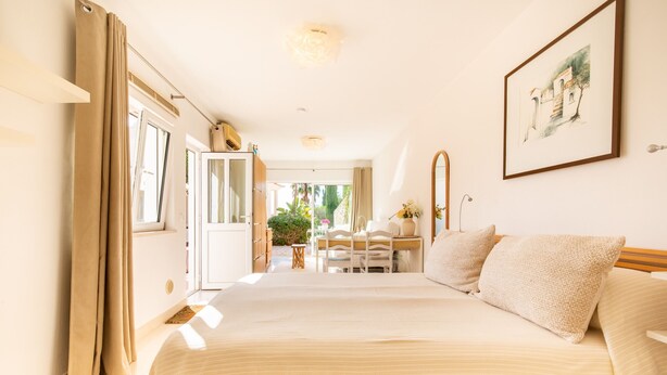A bedroom with a large bed, a desk, and a chair, with a view of a garden through an open door. - Quinta Felicidade, 4 bedroom holiday villa with private pool (Lagos)