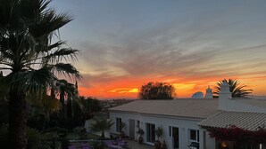 A pool area with lounge chairs, a building with a tiled roof, and a sunset in the background. - Quinta Felicidade, 4 bedroom holiday villa with private pool (Lagos)