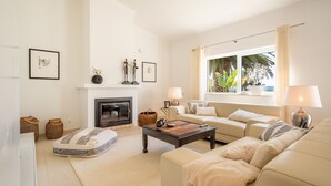 A living room with a fireplace, sofa, coffee table, and a large window with curtains. - Quinta Felicidade, 4 bedroom holiday villa with private pool (Lagos)