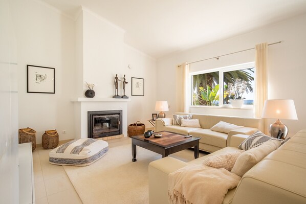 A living room with a fireplace, sofa, coffee table, and a large window with curtains. - Quinta Felicidade, 4 bedroom holiday villa with private pool (Lagos)