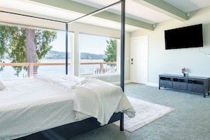 Une chambre avec un grand lit, une vue sur un lac, un balcon, un téléviseur fixé au mur et une commode de couleur sombre.