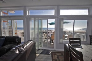 A spacious balcony with a view of the beach, a leather sofa, and a wooden table. - Modern Ship Bottom Oceanfront House with Amazing Ocean Views (Ship Bottom)