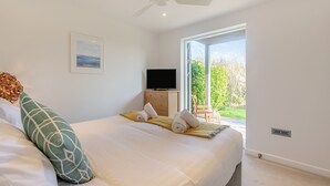 A bedroom with a bed, pillows, a television, a ceiling fan, and a window with a view of greenery. - 1 bedroom accommodation in Carbis Bay, near St Ives (Carbis Bay, near St Ives)