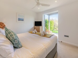 A bedroom with a bed, pillows, a television, a ceiling fan, and a window with a view of greenery. - 1 bedroom accommodation in Carbis Bay, near St Ives (Carbis Bay, near St Ives)