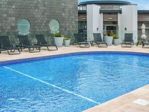 Una piscina con sillas de descanso, plantas en macetas y un edificio moderno con fachada de ladrillo.