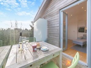 Una mesa de madera con copas de vino, una botella y alimentos en un balcón con vista al interior de una casa.