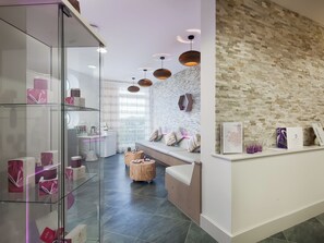 A modern hotel lobby with a glass display case, a reception desk, a seating area, and a textured wall.