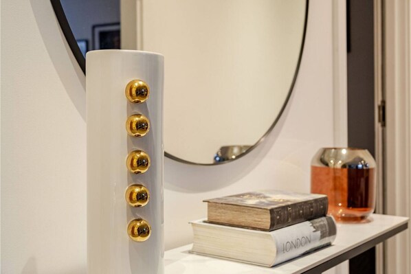 A white cylindrical object with five golden knobs, a mirror, and a small table with books and a glass container.