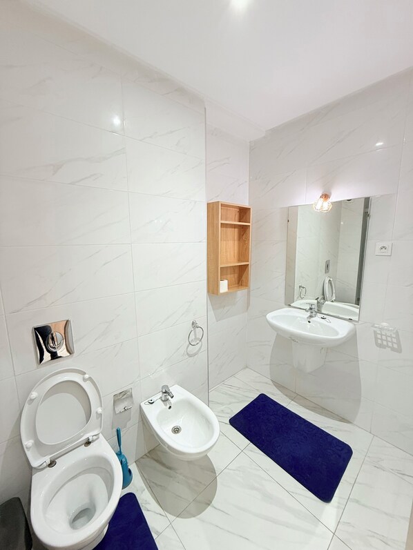 A modern bathroom with a toilet, bidet, sink, and mirror. - Appartement Cosy Vus piscine Familiale (Marrakech)