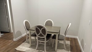Un coin repas avec une table en bois et quatre chaises, un tapis sur le sol et une porte à l’arrière-plan.