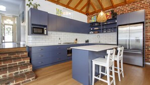 Une cuisine moderne avec des meubles bleus, un îlot central, des chaises blanches et un réfrigérateur en acier inoxydable.