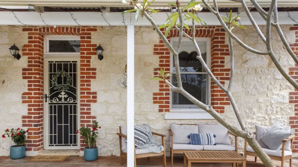 Une terrasse en bois avec un mur en briques, un banc en bois, une table et deux plantes en pot.