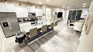 A modern kitchen with white cabinets, stainless steel appliances, and a central island with bar stools. - Our stunning luxury villa, complete with a heated pool, a relaxing hot tub, (Davenport)