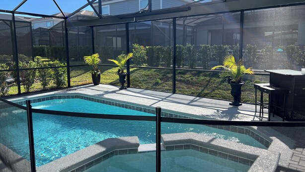 A pool area with a glass enclosure, potted plants, and a patio with outdoor furniture. - Our stunning luxury villa, complete with a heated pool, a relaxing hot tub, (Davenport)