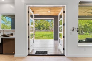 Una cocina moderna con lavavajillas, techo de madera y vista a un jardín césped a través de una puerta abierta.