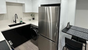Een moderne keuken met roestvrijstalen apparatuur, een zwarte wasmachine en een barkruk.