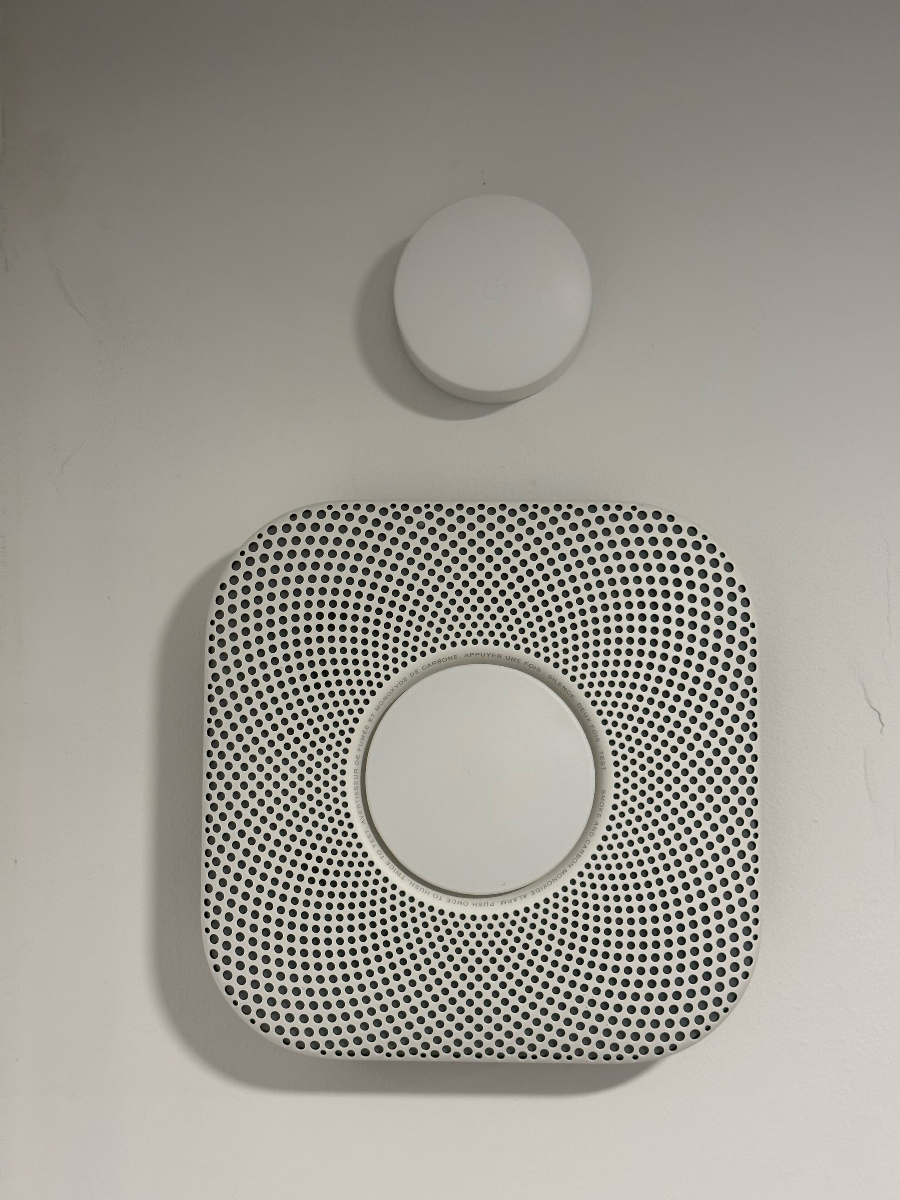 A white, perforated, square-shaped object with a circular hole in the center, placed on a plain surface.